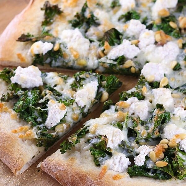 close up shot of kale pine nut and ricotta pizza on wood board