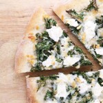 overhead shot of kale pine nut and ricotta pizza on wood board