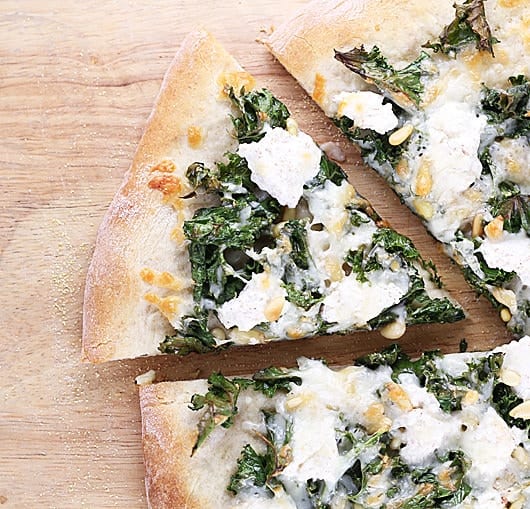 overhead shot of kale pine nut and ricotta pizza on wood board
