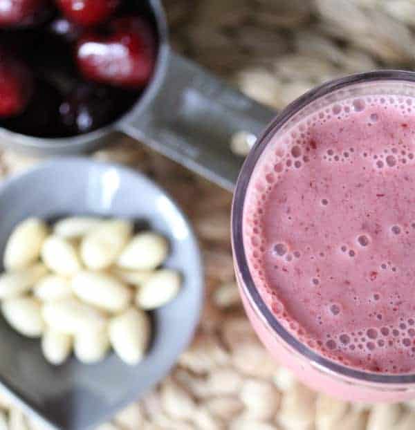 Overhead view of Cherry Almond Smoothie in a glass with a cup of cherries and almonds next to it