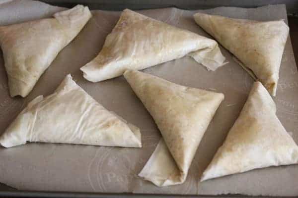 Six Kale Spanakopitas wrapped in phyllo pastry on parchment before baking