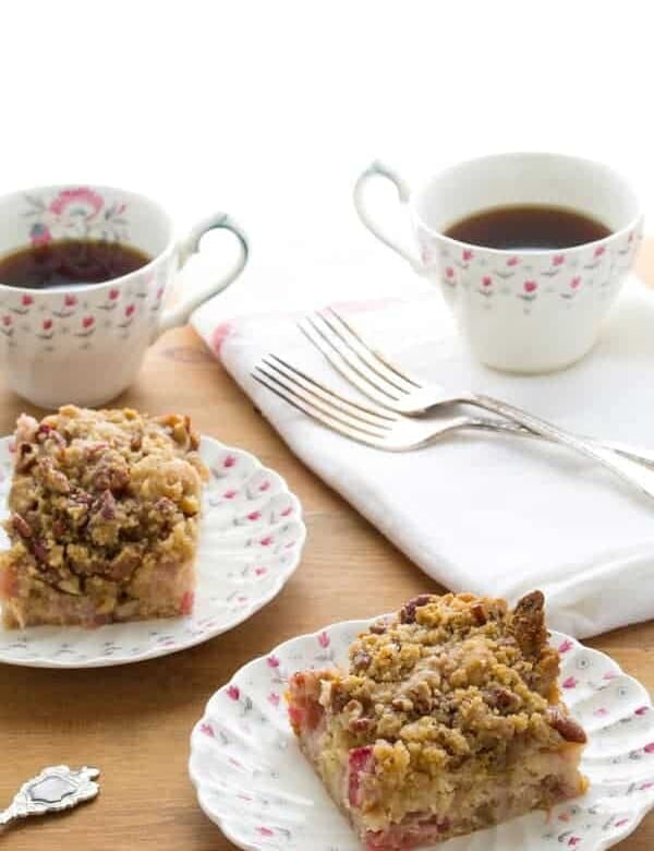 two slices of rhubarb coffee cake with nutmeg and pecan streusel on plates with cups of coffee