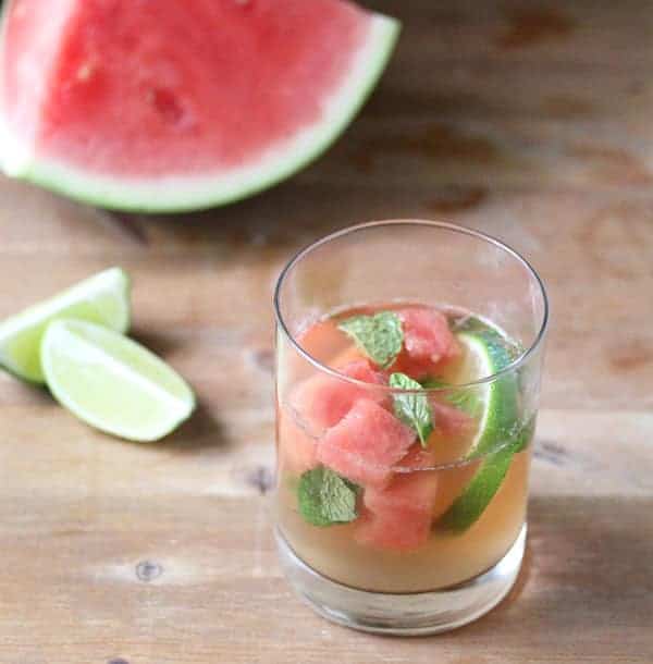 Virgin Watermelon Sangria in a glass with a large slice of watermelon behind it and fresh limes