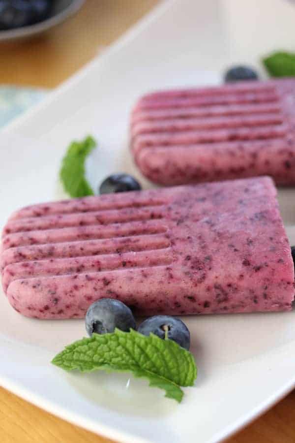 Close up view of Yogurt Popsicles on a white plate with fresh mint and blueberries