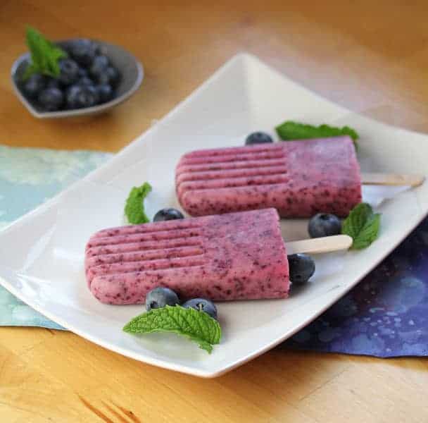 Two Yogurt Popsicles on a white plate with fresh blueberries and mint