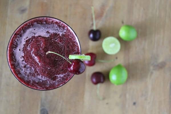 Overhead shot of Frozen Cherry Limeade in glass with fresh limes and cherries next to it