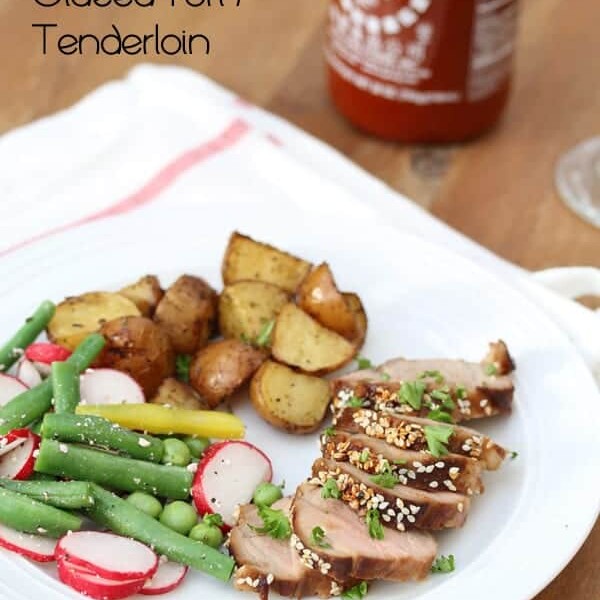 sriracha and sesame glazed pork tenderloin on plate with potatoes and vegetables