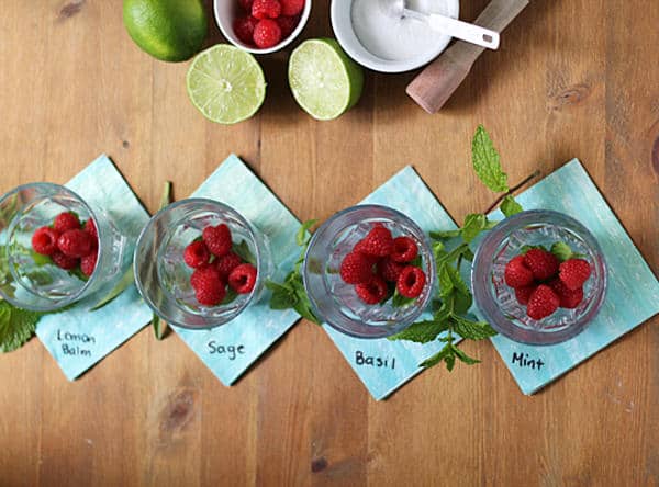 Overhead view of four glasses of Raspberry Smash Cocktail with four herb options of lemon balm, sage, basil, or mint