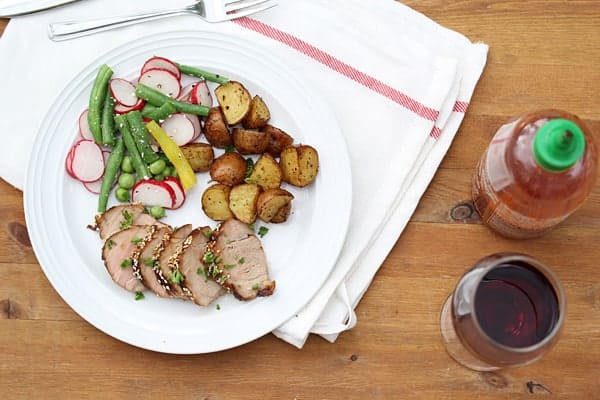 Glazed Pork Tenderloin with roasted potatoes and vegetables on a plate with glass of wine