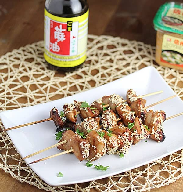 Grilled Chicken Kebabs on white serving plate with bottle of soy sauce and miso paste in the background