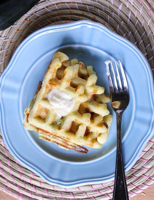 overhead shot of zucchini cheddar and cornmeal waffle on blue plate with fork