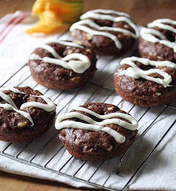 Six Chocolate Zucchini Donuts with white chocolate drizzle cooling on a wire rack