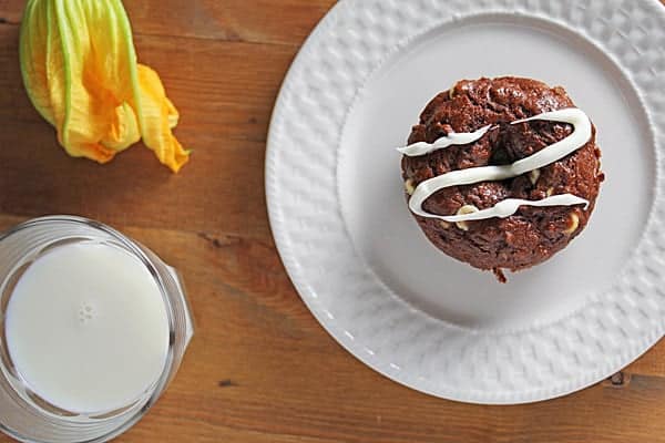 Chocolate Zucchini Donut with white chocolate drizzle on a white plate with a glass of milk