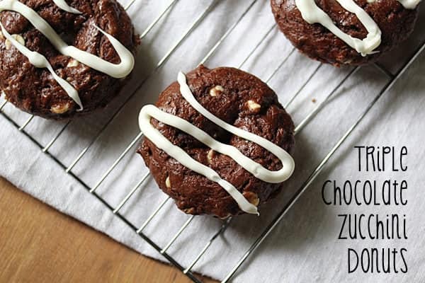 Three Chocolate Zucchini Donuts with white chocolate drizzle on wire rack