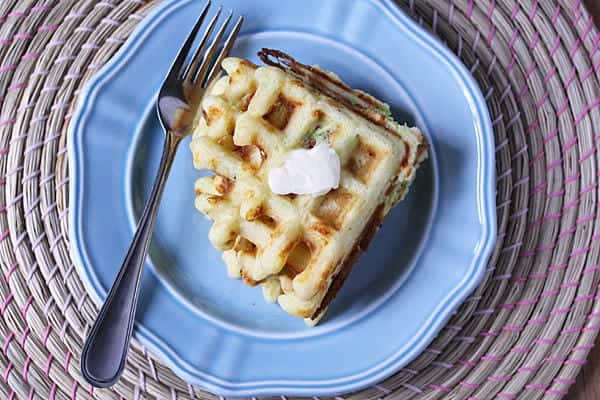 Overhead view of Zucchini and Cheddar Waffleson a blue plate wit ha fork and bite taken out of them