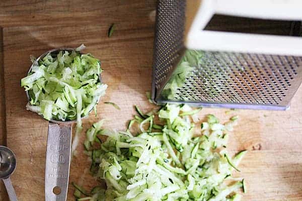 Overhead shot of grated Zucchini on a cutting board next to a grater