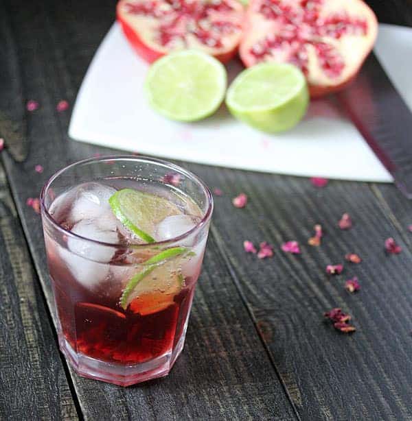 Pomegranate and Rosewater Spritzer in a glass with a fresh pomegrante and lime in the background