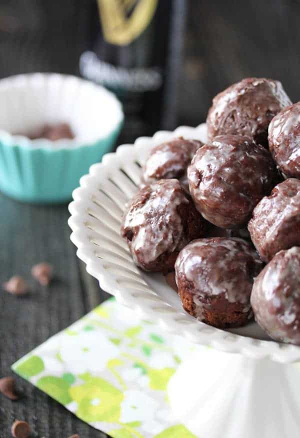 Pile of Chocolate Glazed Donut Holes in a white serving dish on a yellow napkin