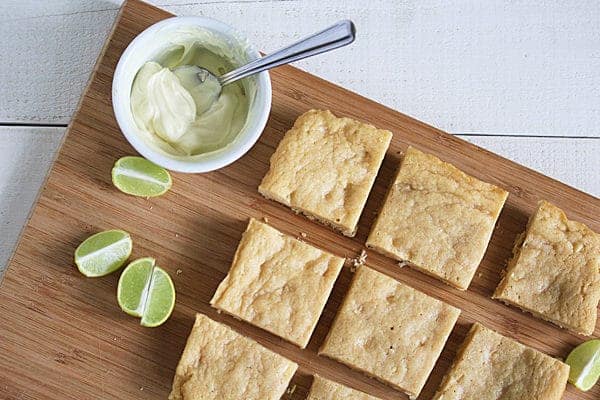 Key Lime Blondies in rows on a wood cutting board with melted white chocolate in ramekin
