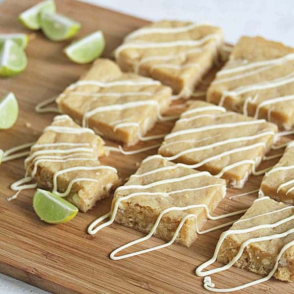 Key Lime Blondies on wood board with white chocolate drizzled and fresh lime wedges