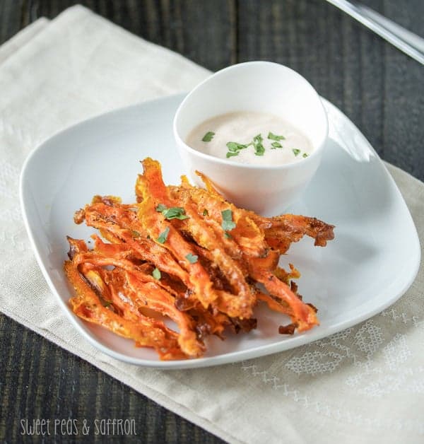 Baked Carrot Chips on a blue serving plate with Harissa Yogurt Dip in a white cup on the side