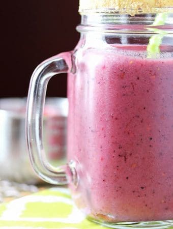 close up of triple berry pie smoothie in mason jar with green straw