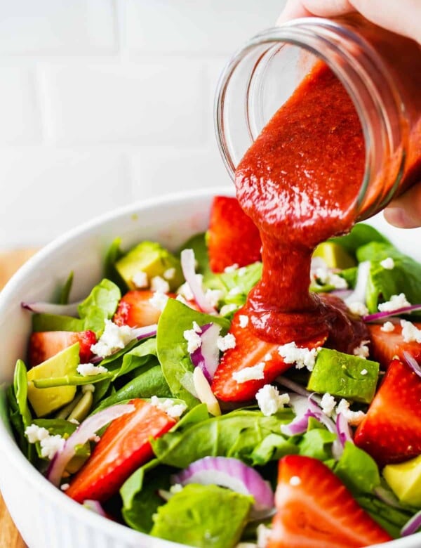 pouring vinaigrette over strawberry spinach salad