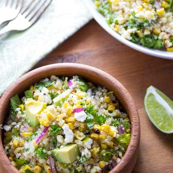 overhead shot of charred corn salad with feta mint and quinoa in wooden bowl with lime wedge
