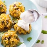 five southwestern baked falafels with corn and black beans on blue plate with spoon putting sour cream on one