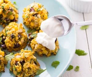 five southwestern baked falafels with corn and black beans on blue plate with spoon putting sour cream on one
