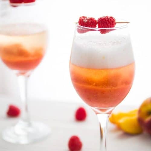 two peach reaspberry bellinis in wine glasses with fresh raspberries