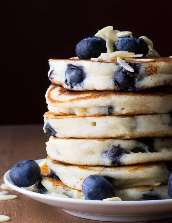 stack of six almond blueberry pancakes with fresh blueberries on plate