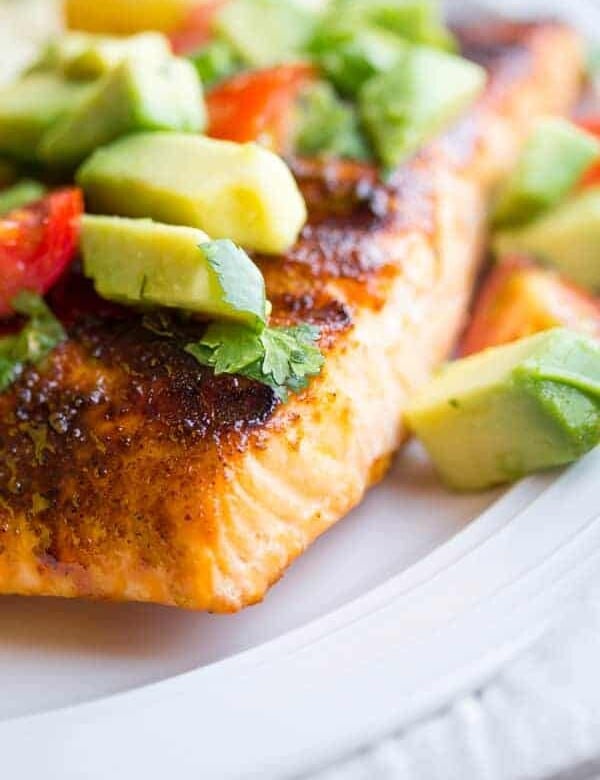 Close up of chili-rubbed salmon on a white plate topped with avocado salsa