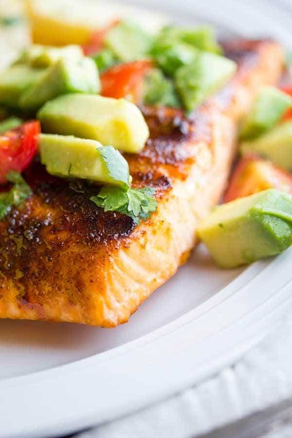 Close up of chili-rubbed salmon on a white plate topped with avocado salsa