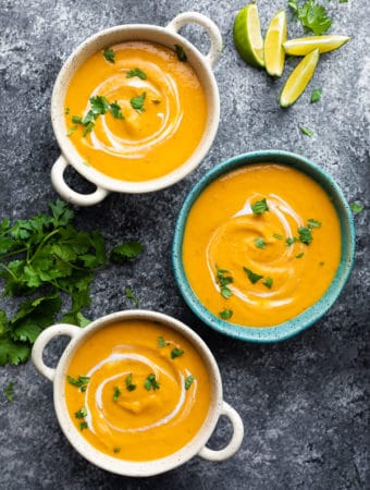 overhead shot of three blue and white bowls filled with thai curry sweet potato soup on gray background