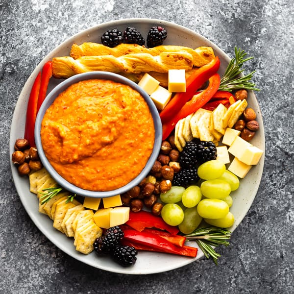 roasted red pepper dip on cheeseboard with grapes, crackers and cheese