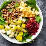 overhead shot of spinach pear salad with gouda and hazelnuts in a large white bowl