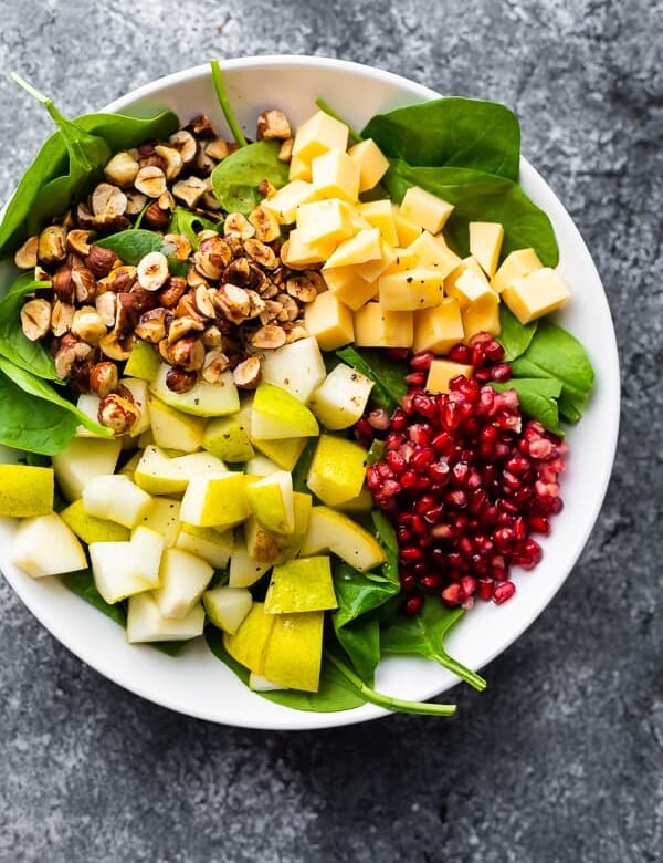 overhead shot of spinach pear salad with gouda and hazelnuts in a large white bowl