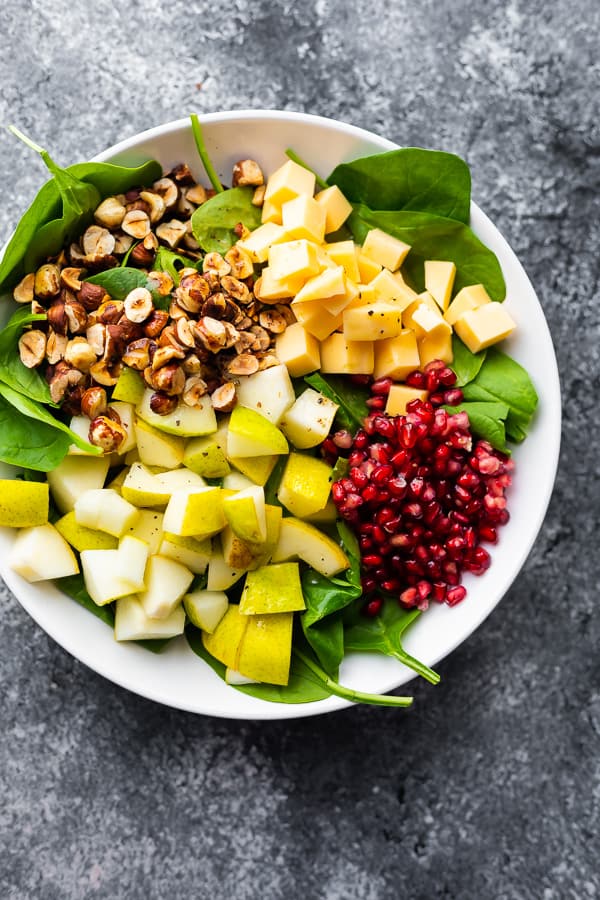 overhead shot of spinach pear salad with gouda and hazelnuts in a large white bowl