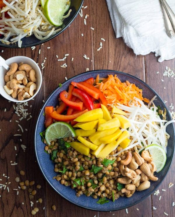 overhead view of two tropical lentil bowls without dressing; bowl of cashews nearby