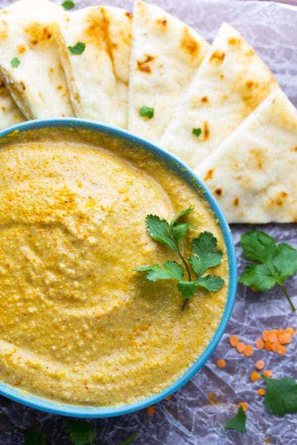 close up overhead view of masala spiced lentil hummus surrounded by naan bread wedges