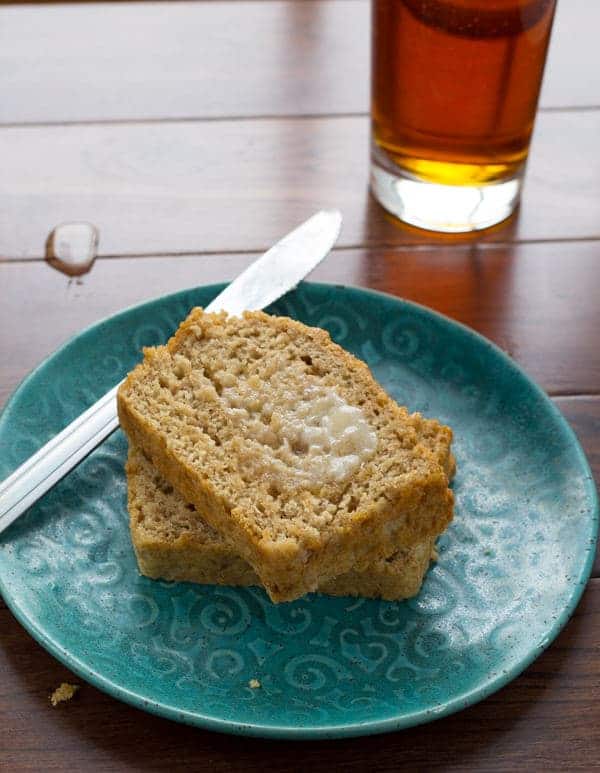 sliced honey rye beer bread with butter spread on it on blue plate with glass of beer in background