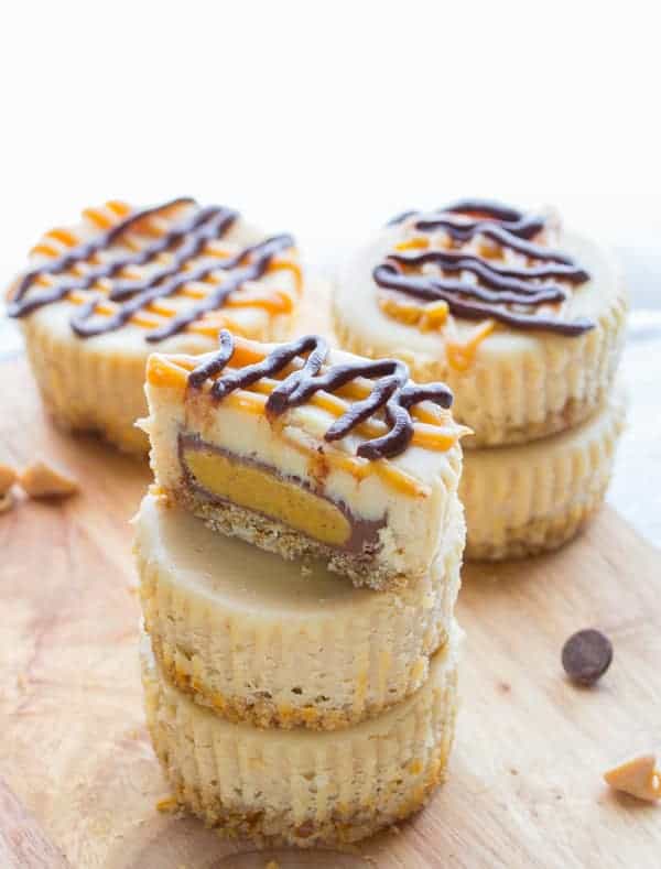 stack of mini Peanut Butter Cup Cheesecakes with Pretzel Crusts with the top one cut in half, revealing a peanut butter cup inside