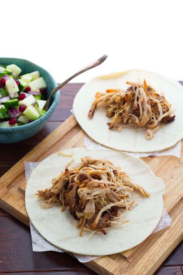 two tortillas topped with apple cider carnitas on wooden cutting board with bowl of apple salsa in background