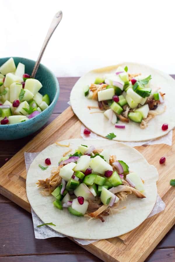 2 tortillas topped with apple cider carnitas and fresh apple salsa on wooden cutting board