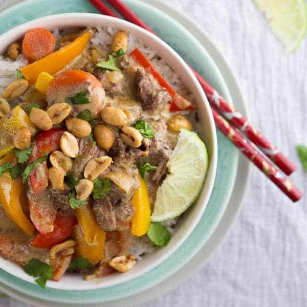 close up view of bowl of thai curry beef on rice with lime wedge