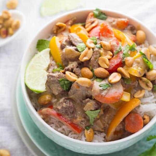 thai curry beef in white bowl with lime slice and peanuts