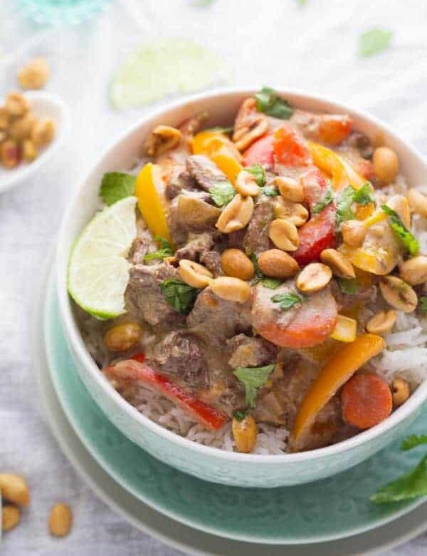 thai curry beef in white bowl with lime slice and peanuts
