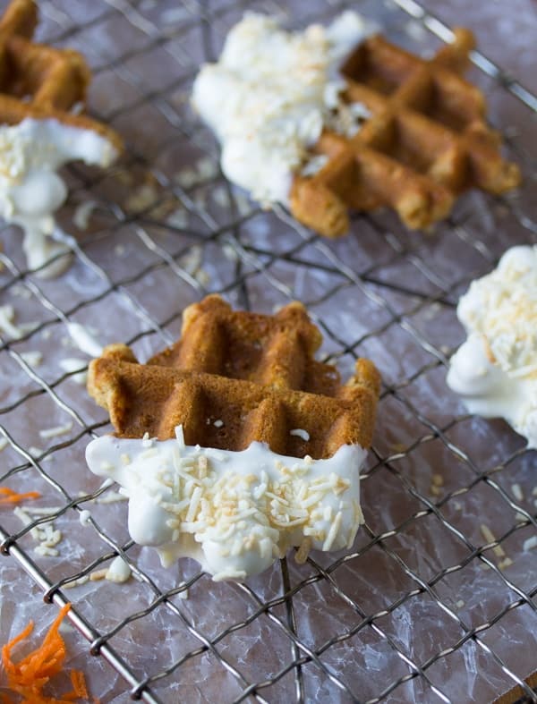 side angle view of carrot cake waffle bites dunked in cream cheese frosting and sitting on wire rack