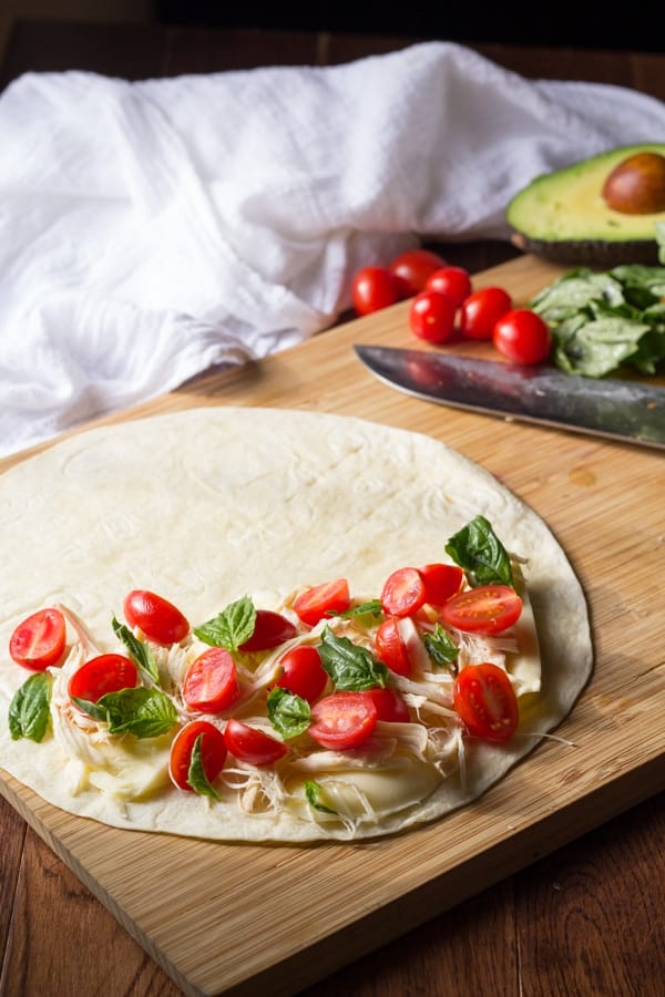 showing how to assemble the caprese quesadilla: cheese, chicken, tomatoes and basil arranged on half a tortilla